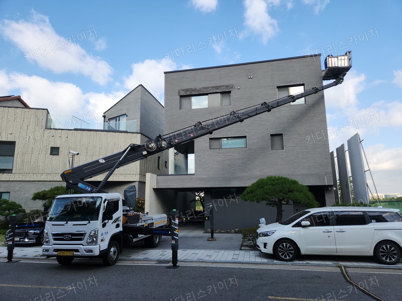 주택 외벽 앞에 붐대와 작업대를 펼친 스카이차